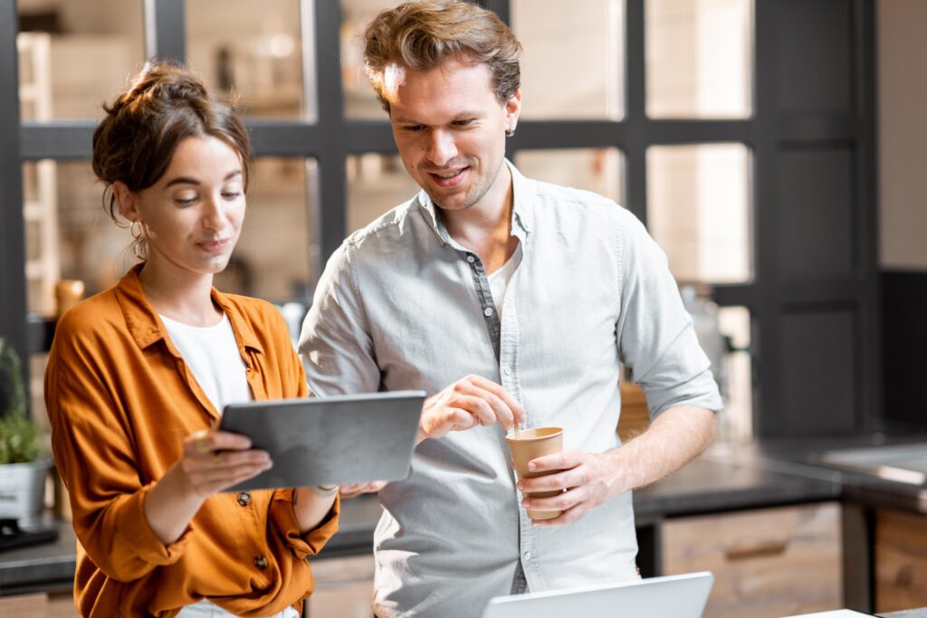 a man and woman standing next to each other looking at an ipad