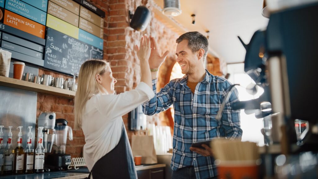 A woman and man behind the counter at a coffee shop giving each other a high five.