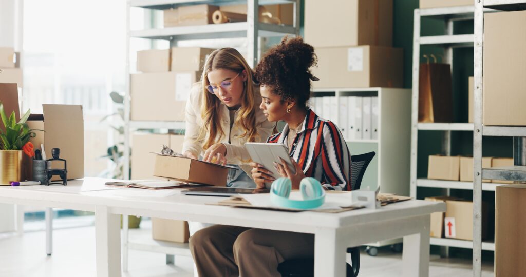 Two Women sitting behind a desk reading and pointing to something on a clipboard.