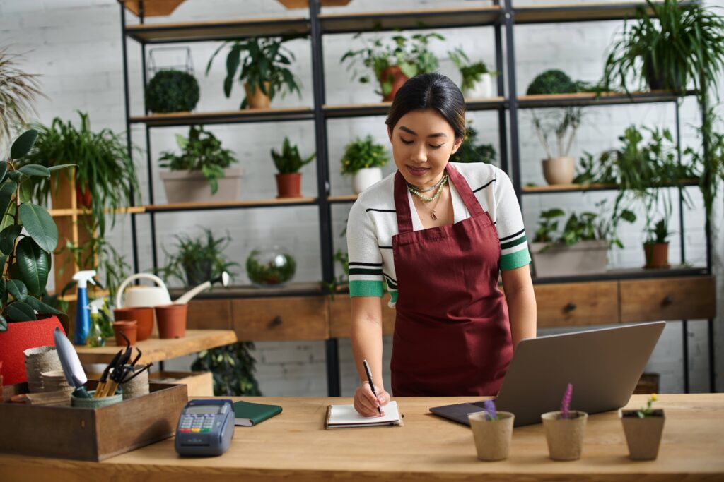 A woman at work in an apron standing behind a counter writing down something in a notepad.